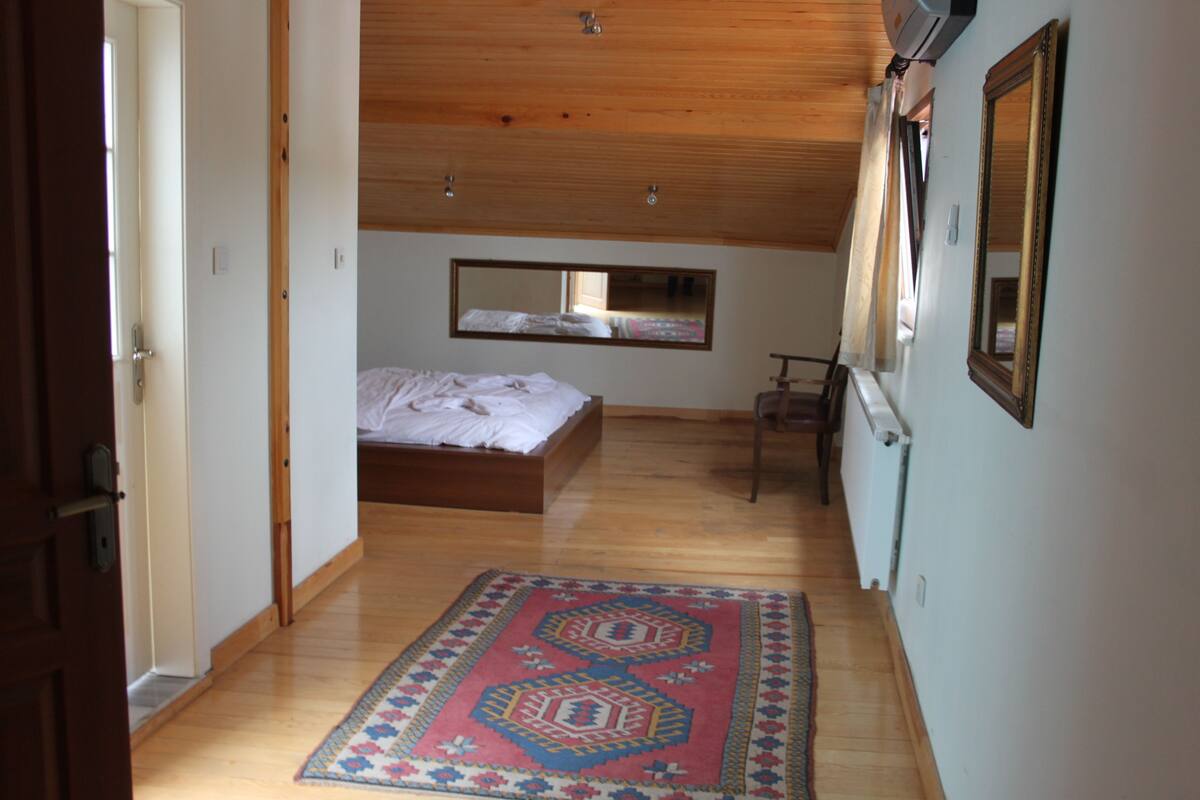 A bedroom with a wooden ceiling, a bed, a mirror, and a patterned rug.