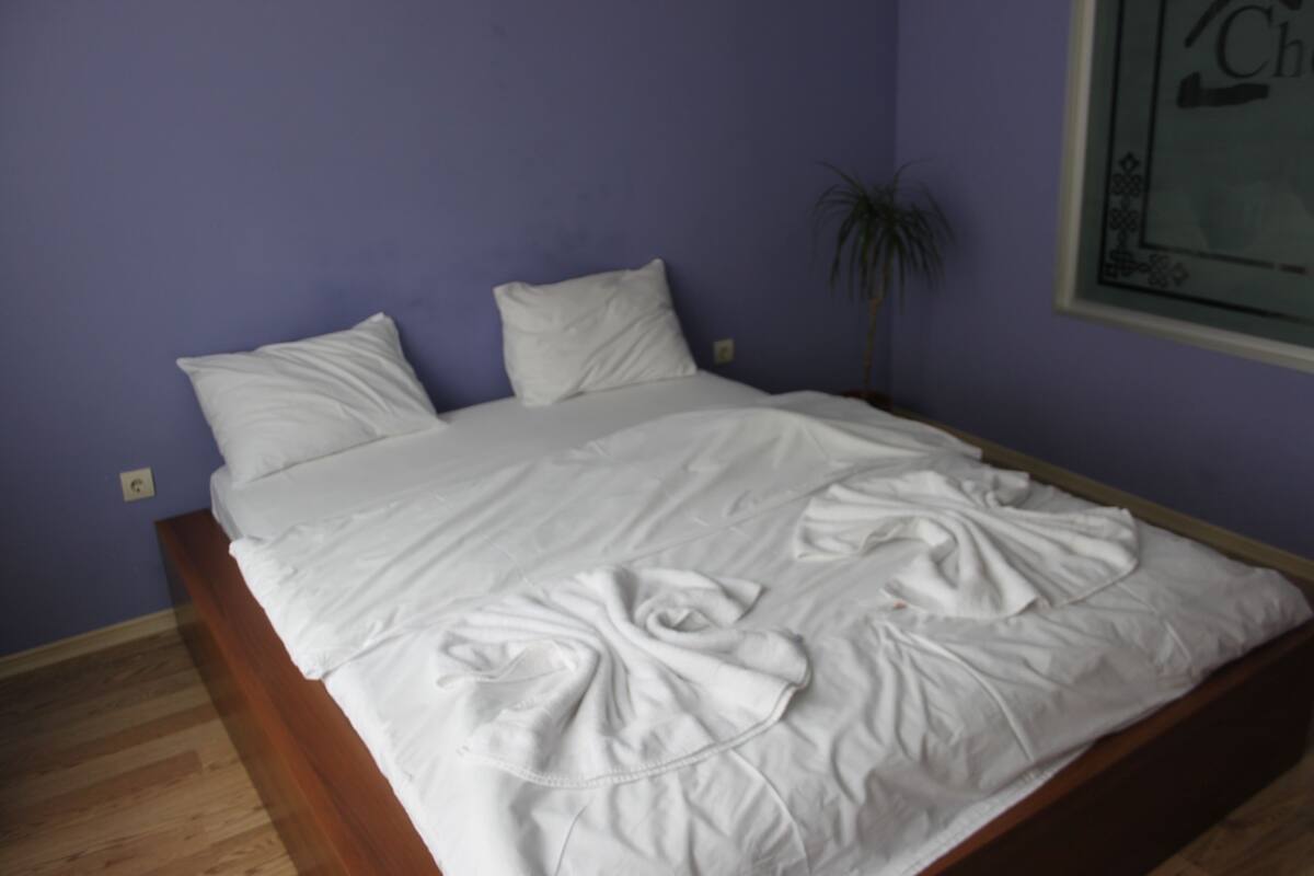 A bedroom with a wooden bed frame, white bedding, and a potted plant.
