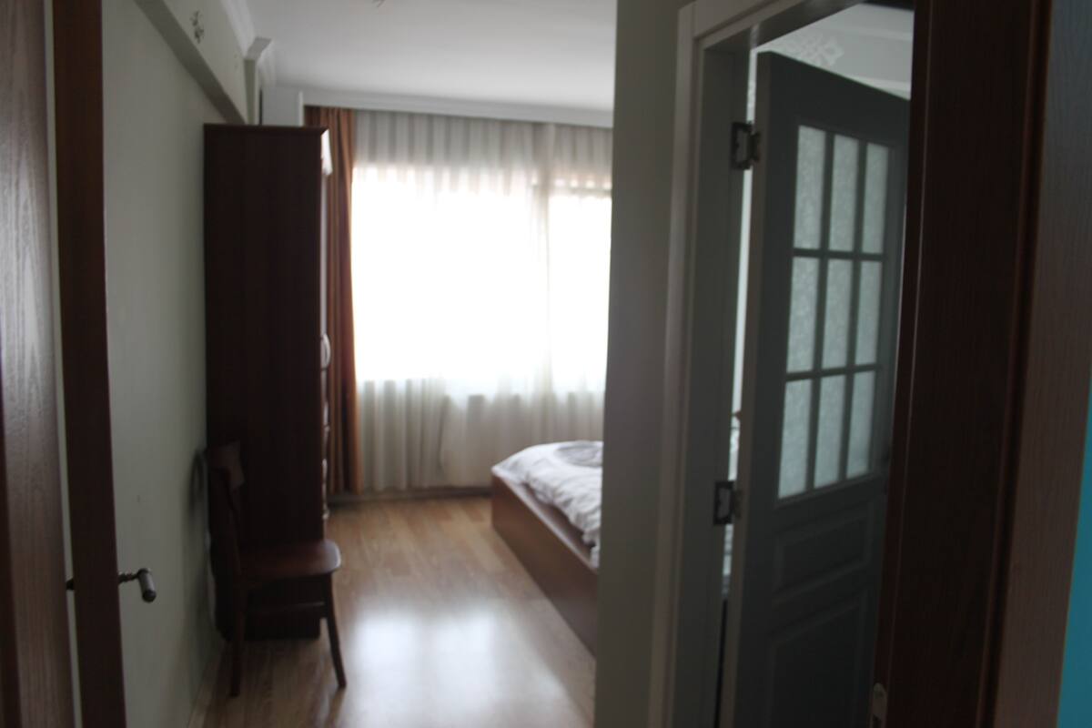 A bedroom with a wooden wardrobe, a bed, and a window with curtains.