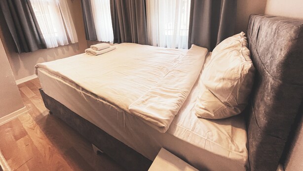 A neatly made bed with a pillow and a folded towel, a flat-screen TV mounted on the wall, and a window with curtains. - Piya Boutique Hotel (Istanbul)