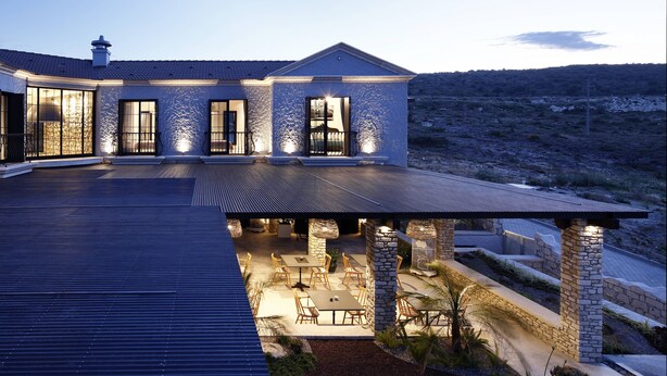 Una casa moderna con un amplio patio, pilares de piedra y una zona de estar cubierta al aire libre.