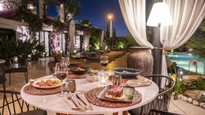 An outdoor dining area with tables set for a meal, surrounded by greenery and a pool. - Alacati Port Ladera Hotel - Adults Only (Cesme)