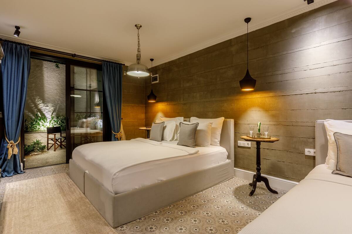 Un dormitorio moderno con una cama grande, una mesita con un florero y vistas a un balcón con plantas.