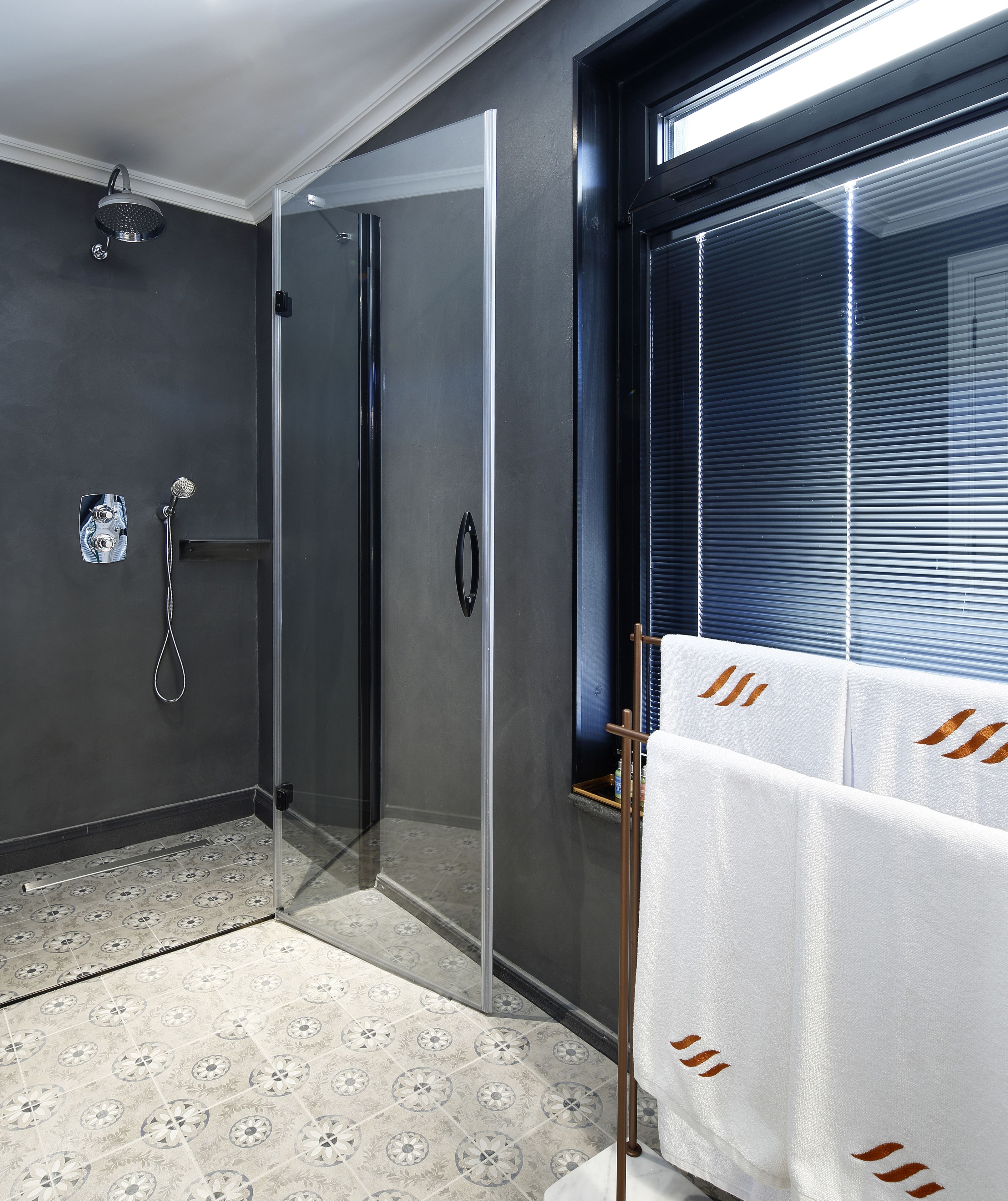A modern bathroom with a glass-enclosed shower, a towel rack, and a window with blinds.