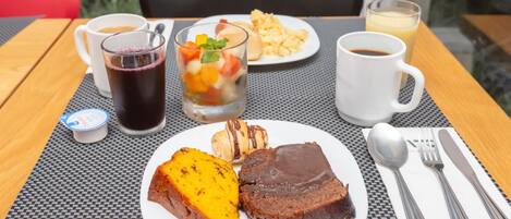A table with a plate of food, a glass of dark liquid, a glass of yellow liquid, a cup of coffee, and a small container of yogurt.