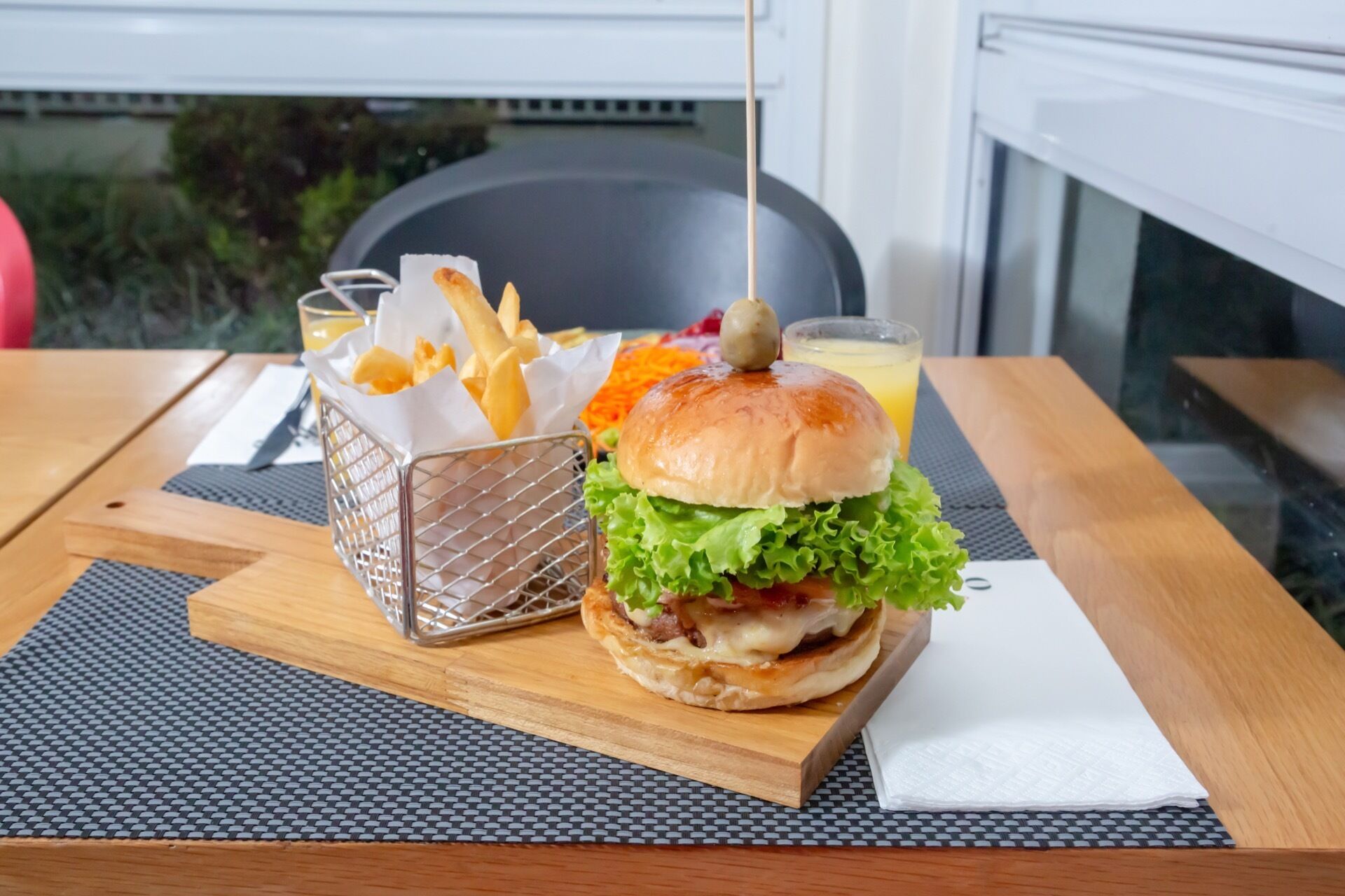 A burger with lettuce and a bun, a basket of fries, and a drink on a table with a placemat.