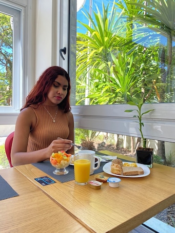 A person sitting at a table with a meal, a window with a view of greenery, and a small potted plant on the table.