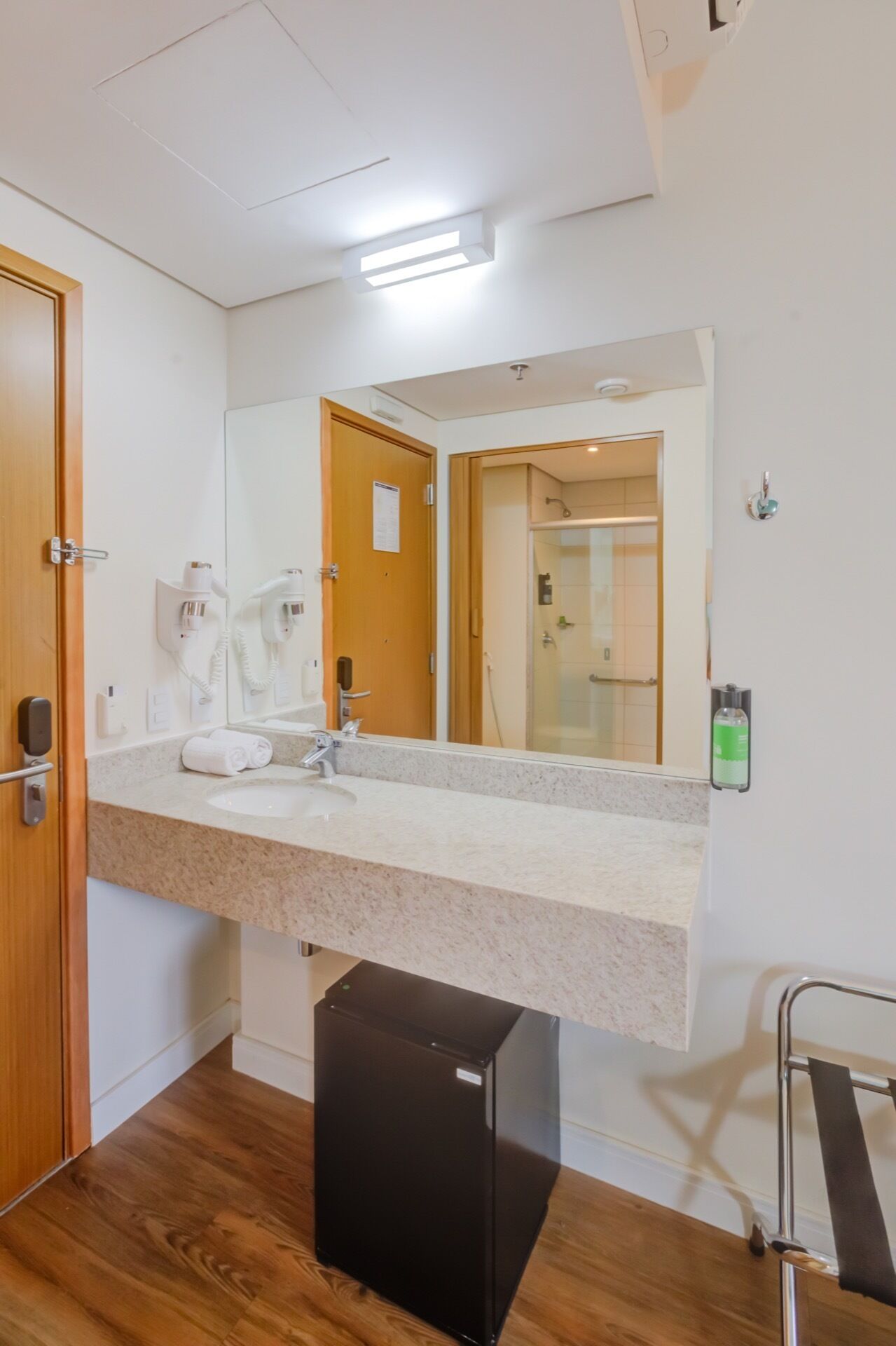 Uma casa de banho moderna com um espelho grande, uma pia e um chuveiro visível através da porta de vidro.