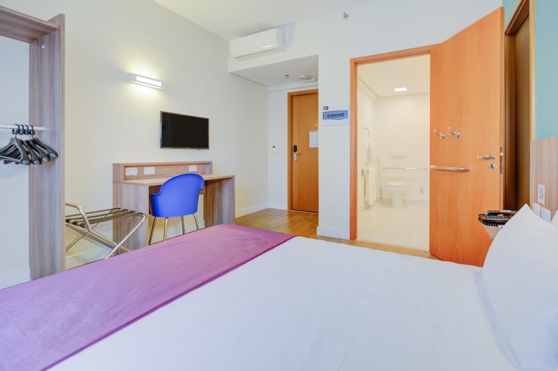 A hotel room with a bed, a desk, a chair, and a television.