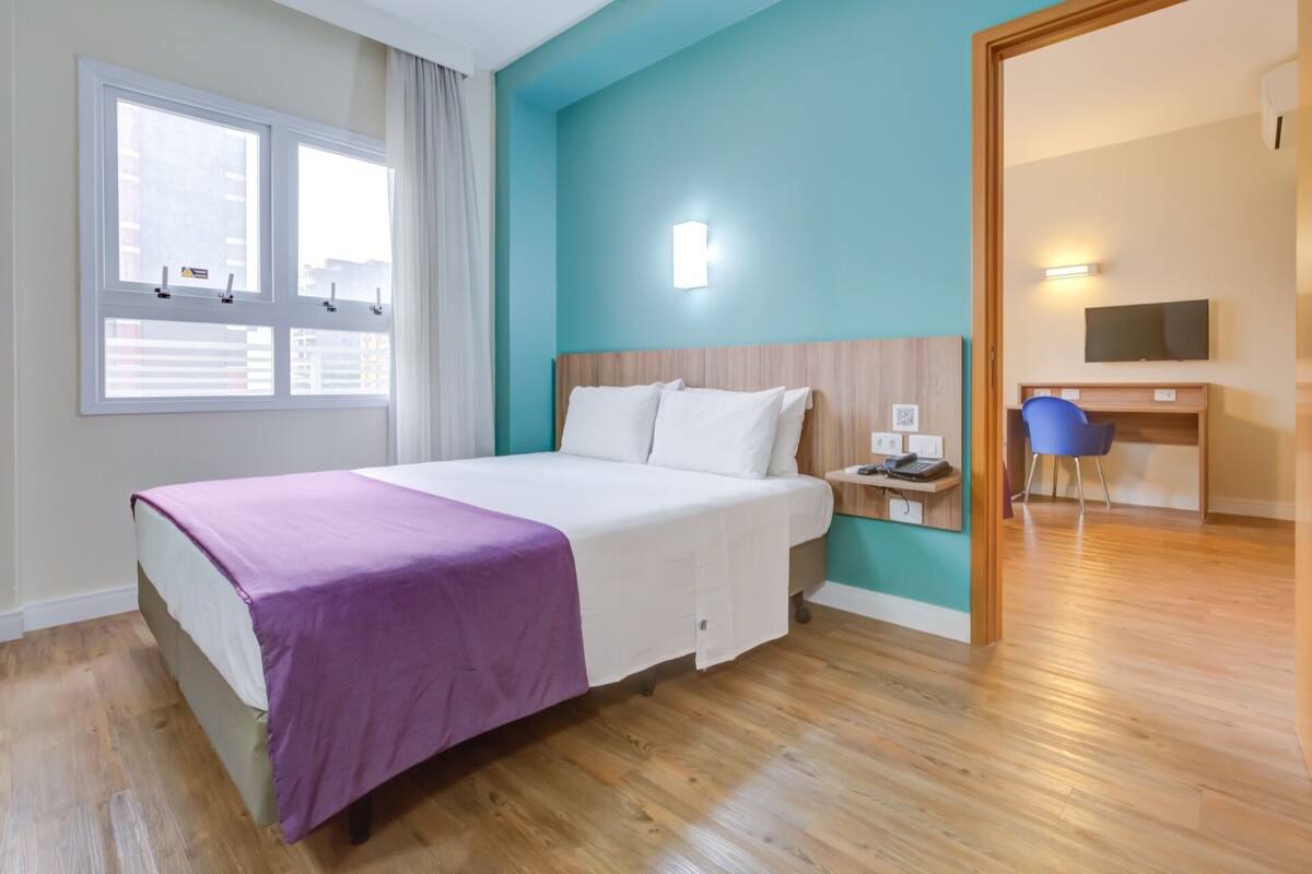Une chambre d’hôtel avec un lit, un bureau, une chaise et un téléviseur.