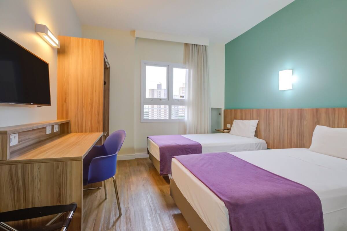 Une chambre d’hôtel avec deux lits, un bureau, une chaise et une télévision.