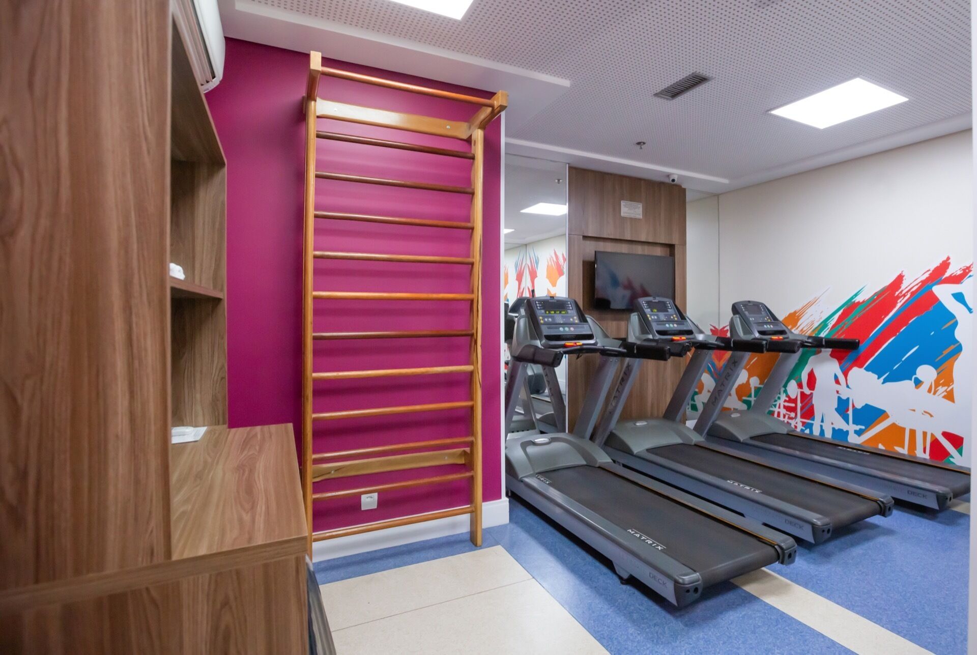 A gym with treadmills, a wooden climbing wall, and a colorful mural.
