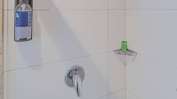 Un espacio de ducha con cabezal de ducha manual, dispensador de jabón y un pequeño plato verde para jabón.