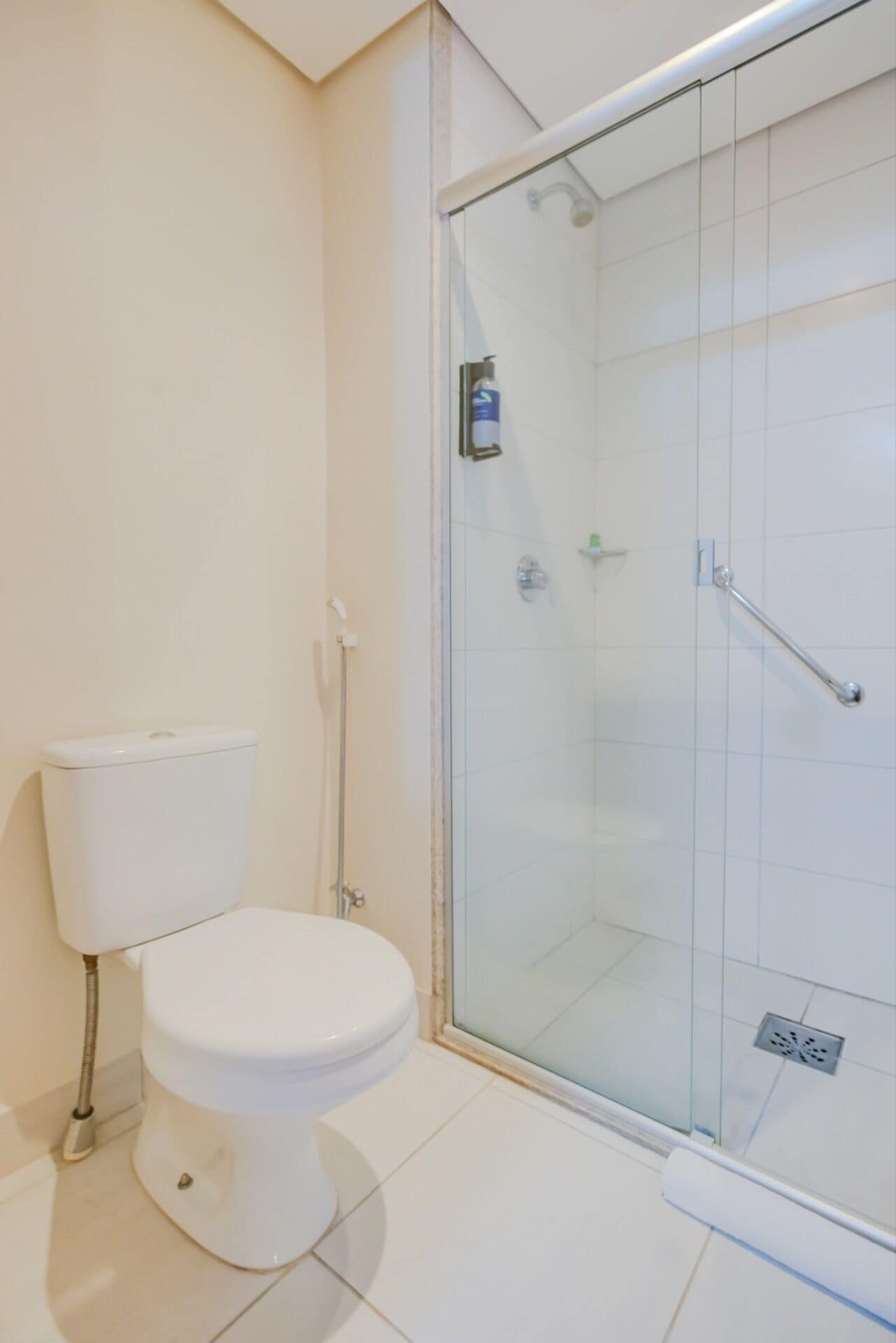 Un baño moderno con inodoro, ducha envuelta en vidrio y suelo de baldosas blancas.