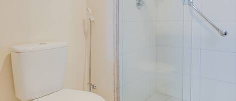 Un baño moderno con inodoro, ducha envuelta en vidrio y suelo de baldosas blancas.