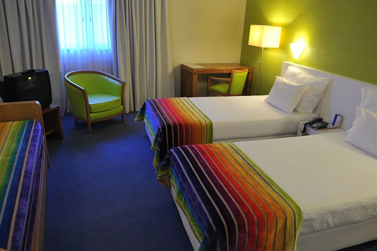 A hotel room with two beds, a television, a chair, a table, and a lamp.