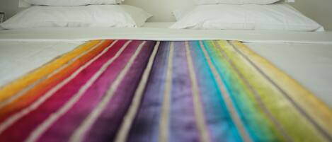 A bed with white linens and a rainbow-striped blanket.