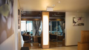Un moderno vestíbulo de hotel con mostrador de recepción de madera, zona de estar con sillones y un amplio ventanal con cortinas.