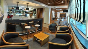 Zona de bar con taburetes, una barra y un área de estar con sillas y una mesa.