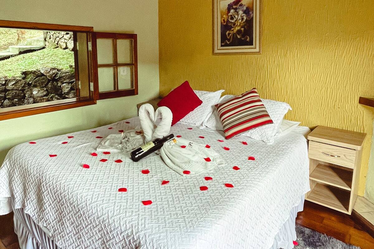 A bedroom with a bed, wooden headboard, a nightstand, a window with a view, and a ceiling fan.