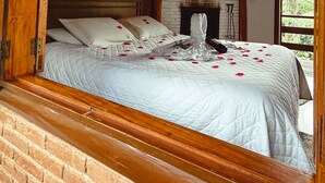 Une chambre à coucher au style rustique, avec un mur en briques, des poutres en bois au plafond et un lit parsemé de pétales de roses.