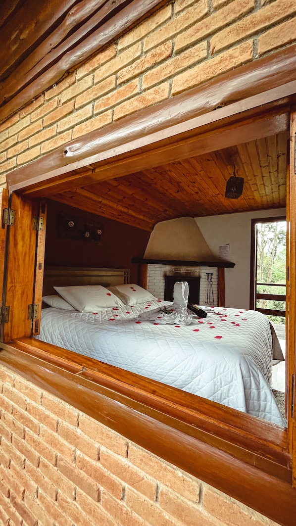 A rustic bedroom with a brick wall, wooden ceiling beams, and a bed with rose petals. - Hotel Pião Mineiro (Camanducaia)