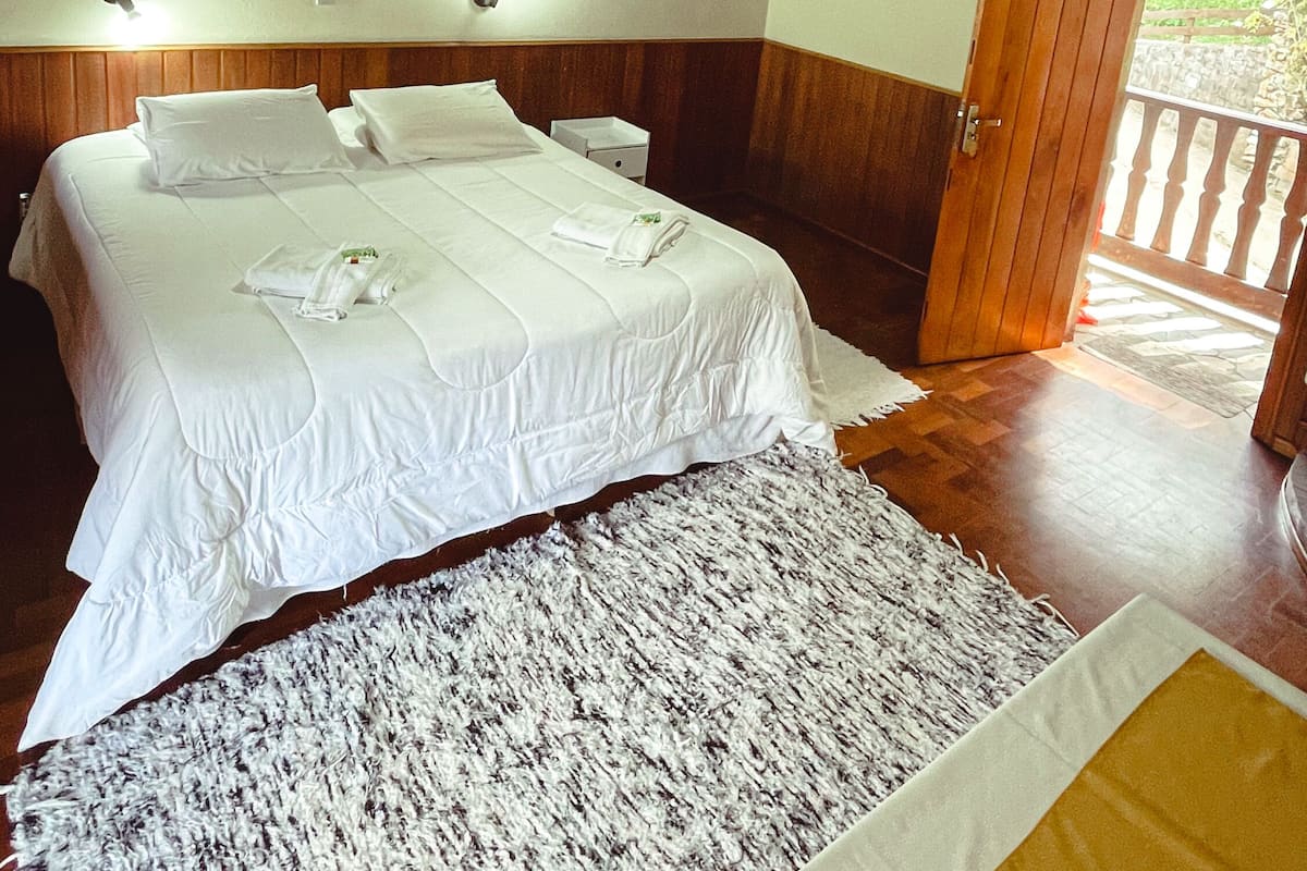 A hotel room with a large bed, a wooden door, and a view of the outdoors.