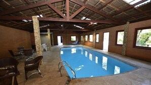 Une piscine intérieure dotée d’un sol en pierre, de poutres en bois et de quelques fauteuils en osier.