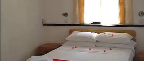 A neatly made bed with a red and white bedspread, two pillows, and two folded towels. A wooden nightstand is beside the bed.