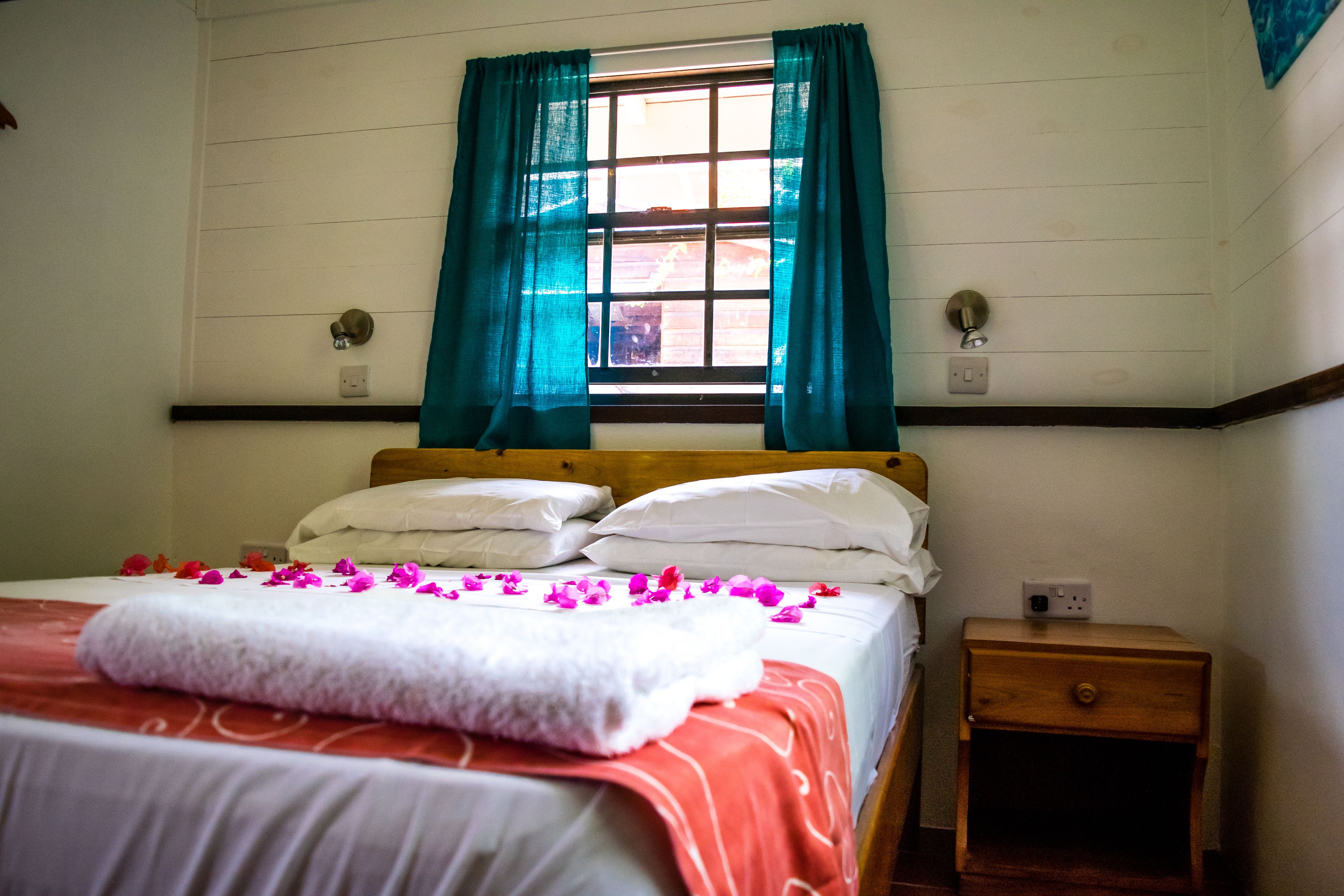 Una habitación de hotel con cama, mesita de noche y ventana con cortinas.