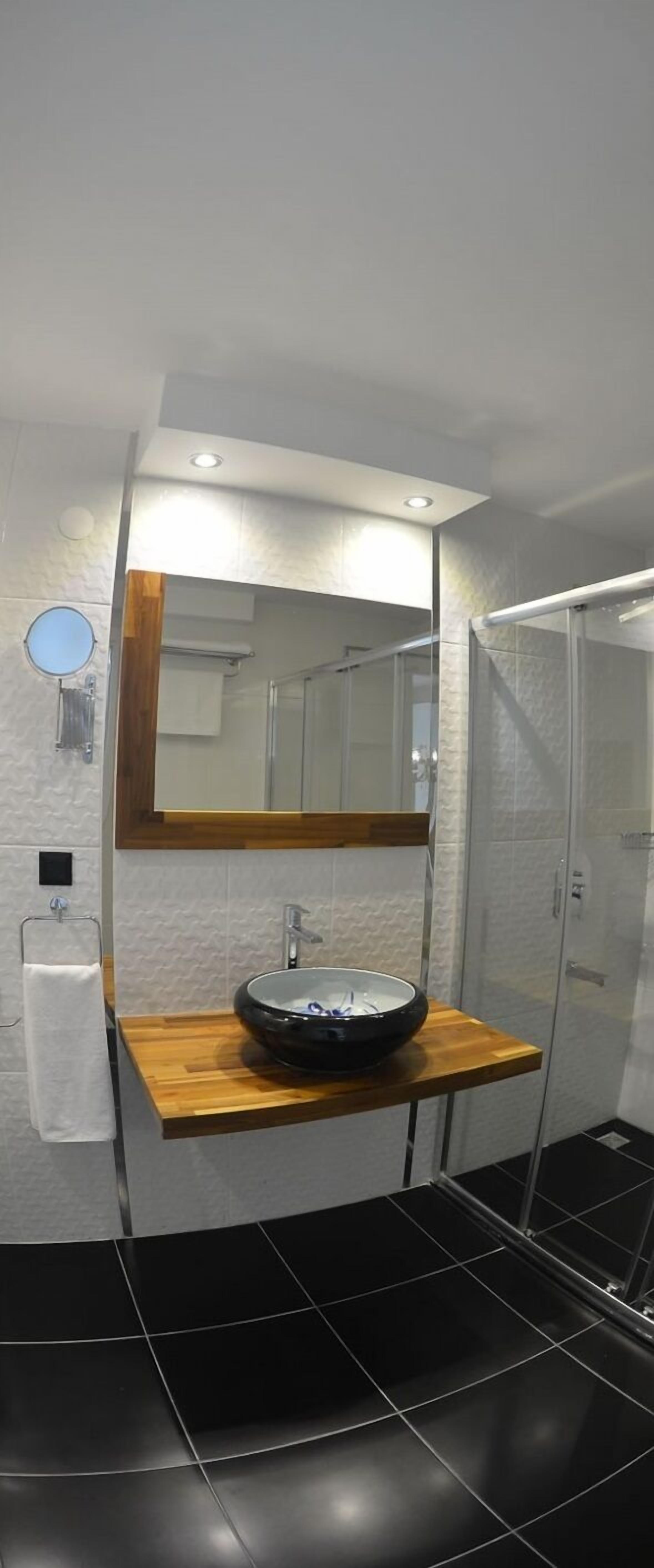 Une salle de bain moderne avec un lavabo rond, un miroir au-dessus et une cabine de douche en verre.