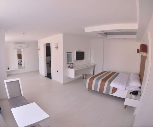 Habitación de hotel moderna con cama, escritorio, televisor y baño visible a través de una puerta abierta.