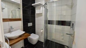 Ein modernes Badezimmer mit einem weißen Waschbecken, schwarz-weißen Fliesen, einer Duschkabine aus Glas und einer Holzauslage.