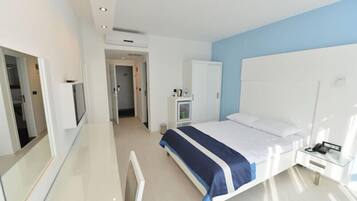 A modern hotel room with a large bed, a bedside table, a wardrobe, and a bathroom visible through an open door.