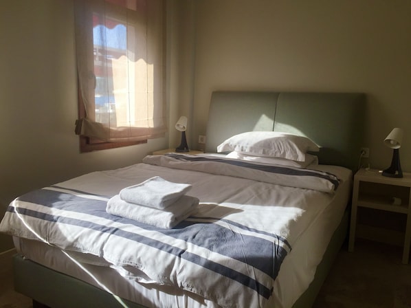 Un lit bien fait, avec une literie à rayures et une serviette pliée, une lampe de chevet et une fenêtre avec des rideaux.