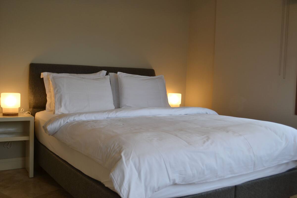 Ein ordentlich gemachtes Bett mit weißer Bettwäsche und je einer Nachttischlampe auf beiden Seiten.