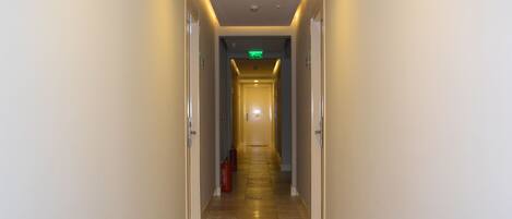 A hotel hallway with a light-colored floor, doors on both sides, and an exit sign at the end.
