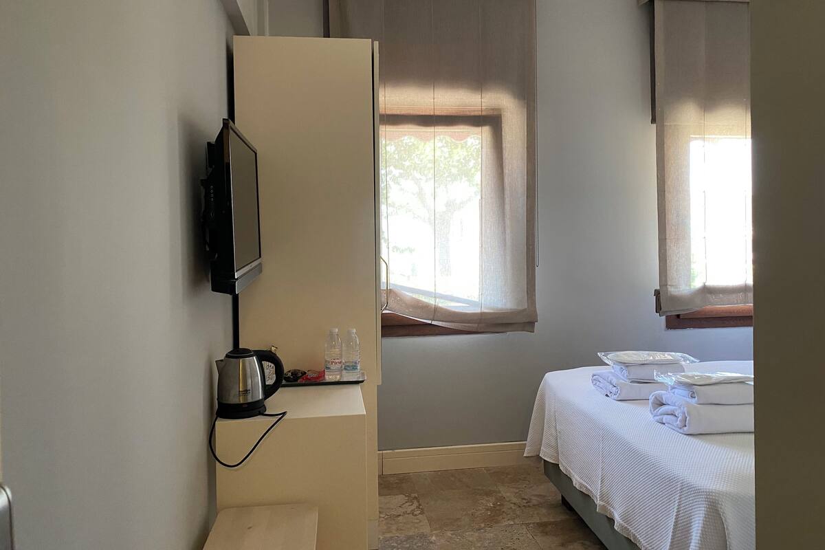 Ein Hotelzimmer mit Bett, Fernseher, Wasserkocher und einem Fenster mit Vorhängen.
