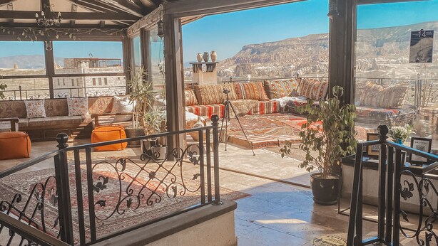 A rooftop terrace with a sofa, cushions, and a view of a mountainous landscape.