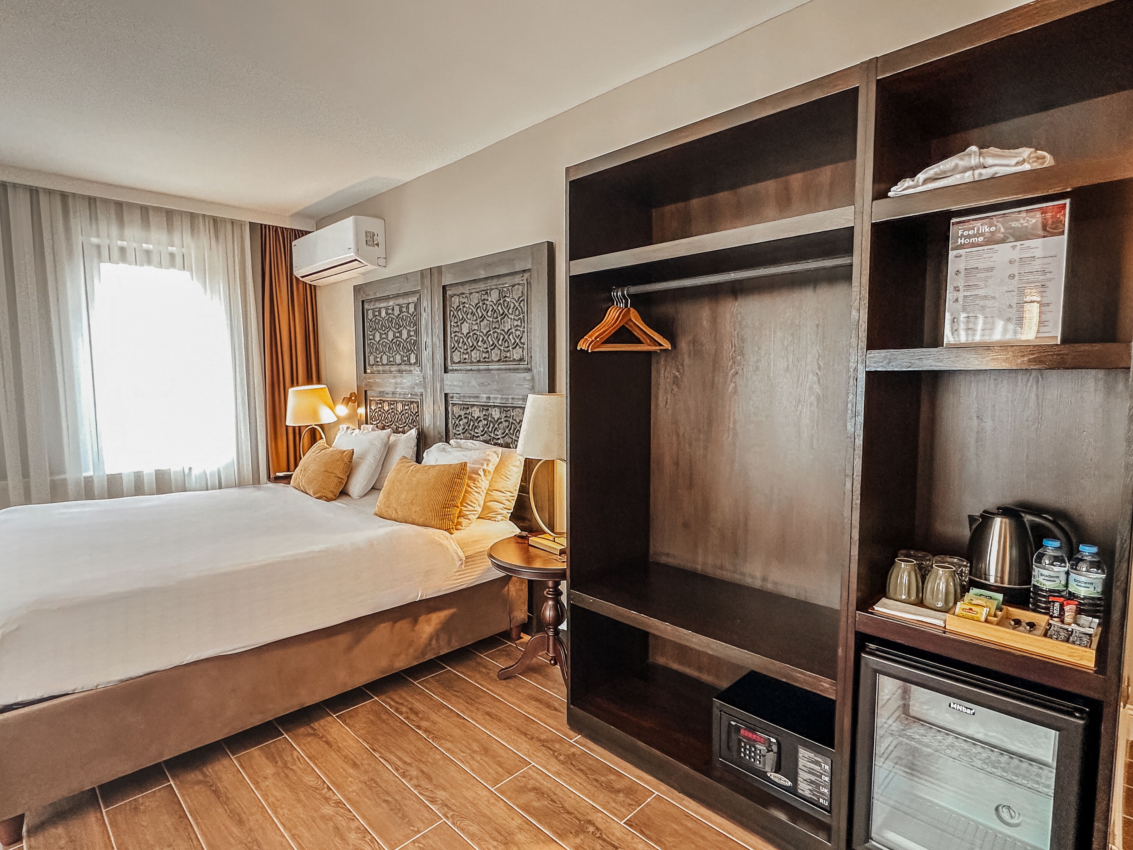 A hotel room with a large bed, a wardrobe, a minibar, and a window with curtains.