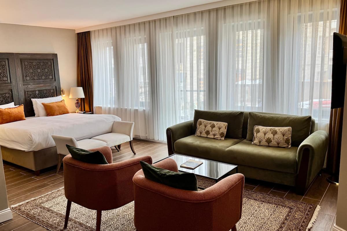 A hotel room with a bed, a sofa, two armchairs, a coffee table, and a television.
