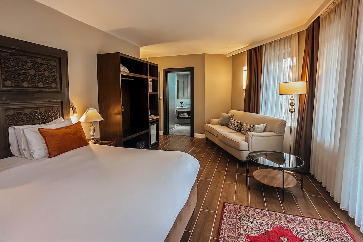 A hotel room with a large bed, a sofa, a small table, and a wardrobe.