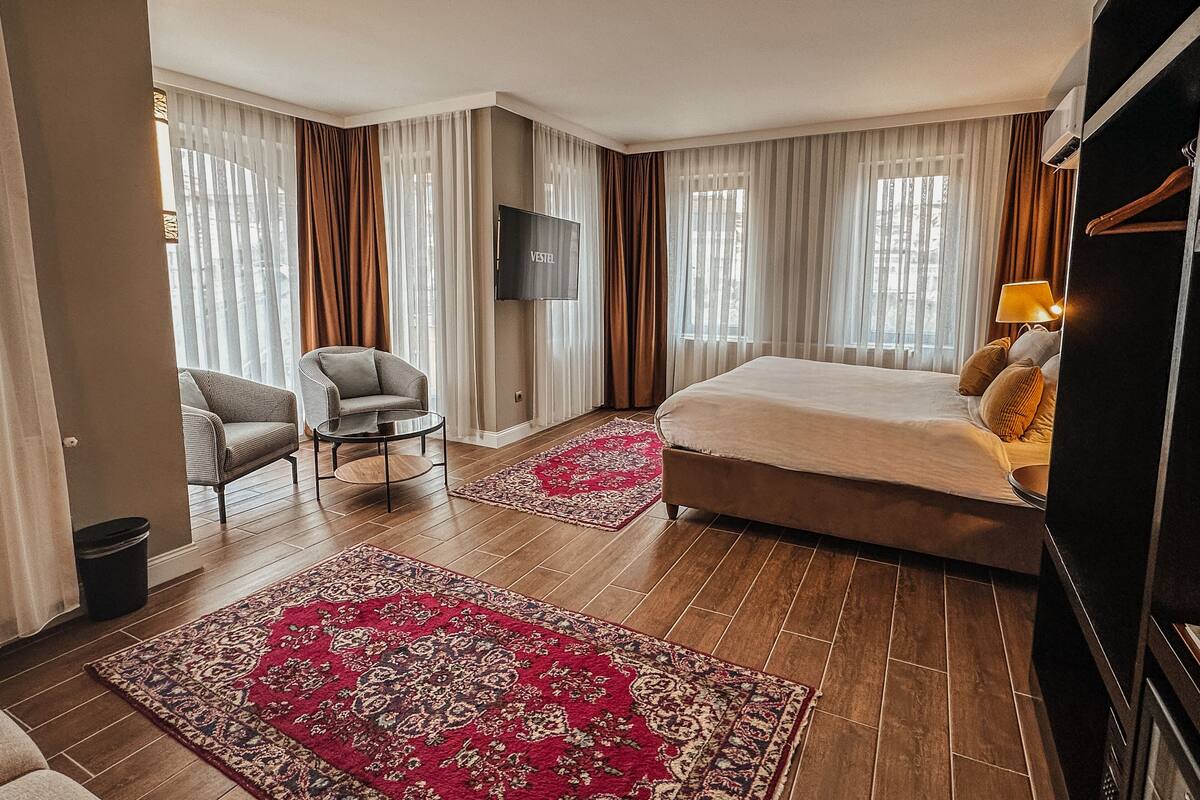 A hotel room with a bed, a chair, a TV, and a large window with curtains.