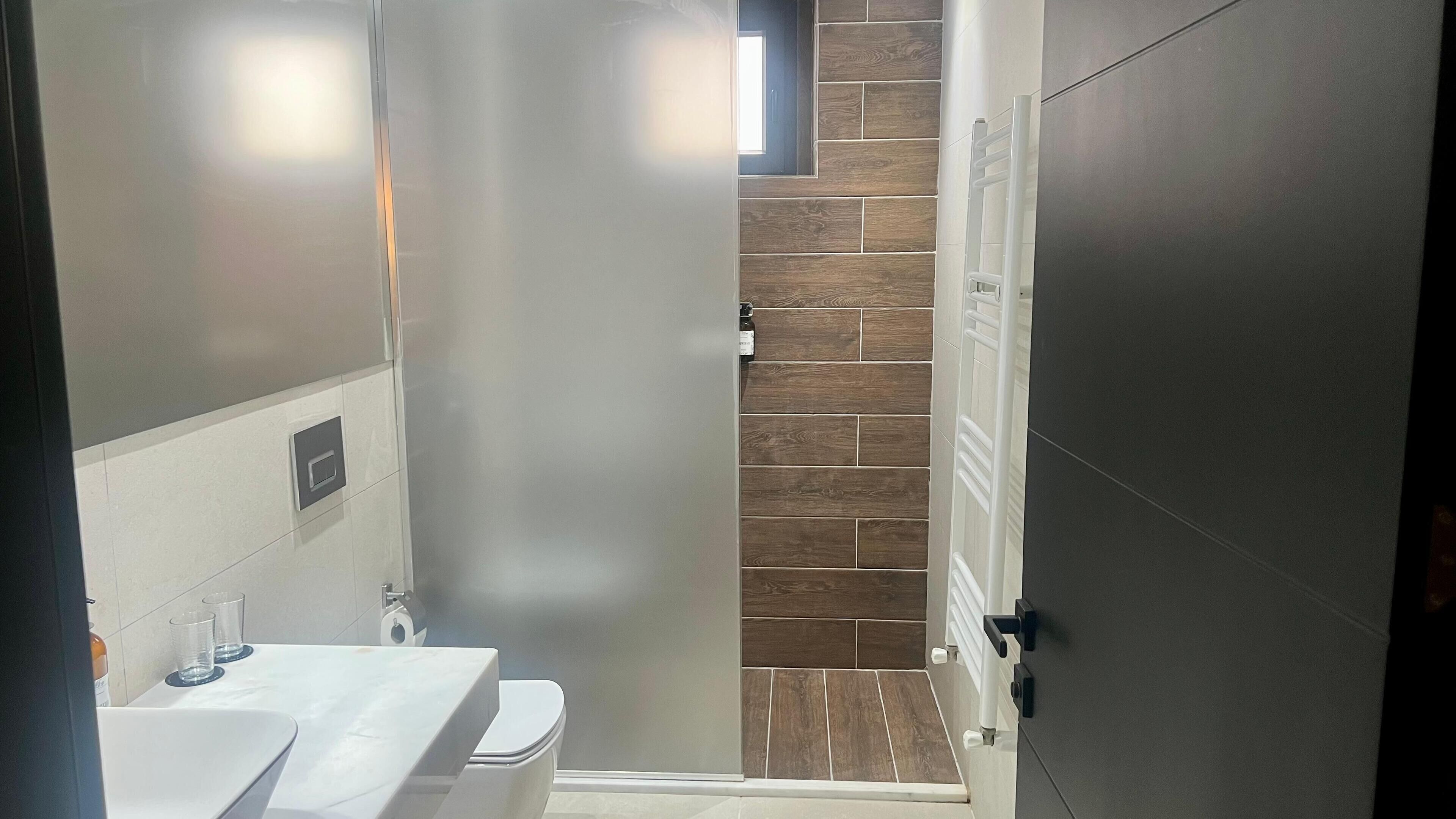 A bathroom with a white sink, toilet, and a shower area with wooden tiles.