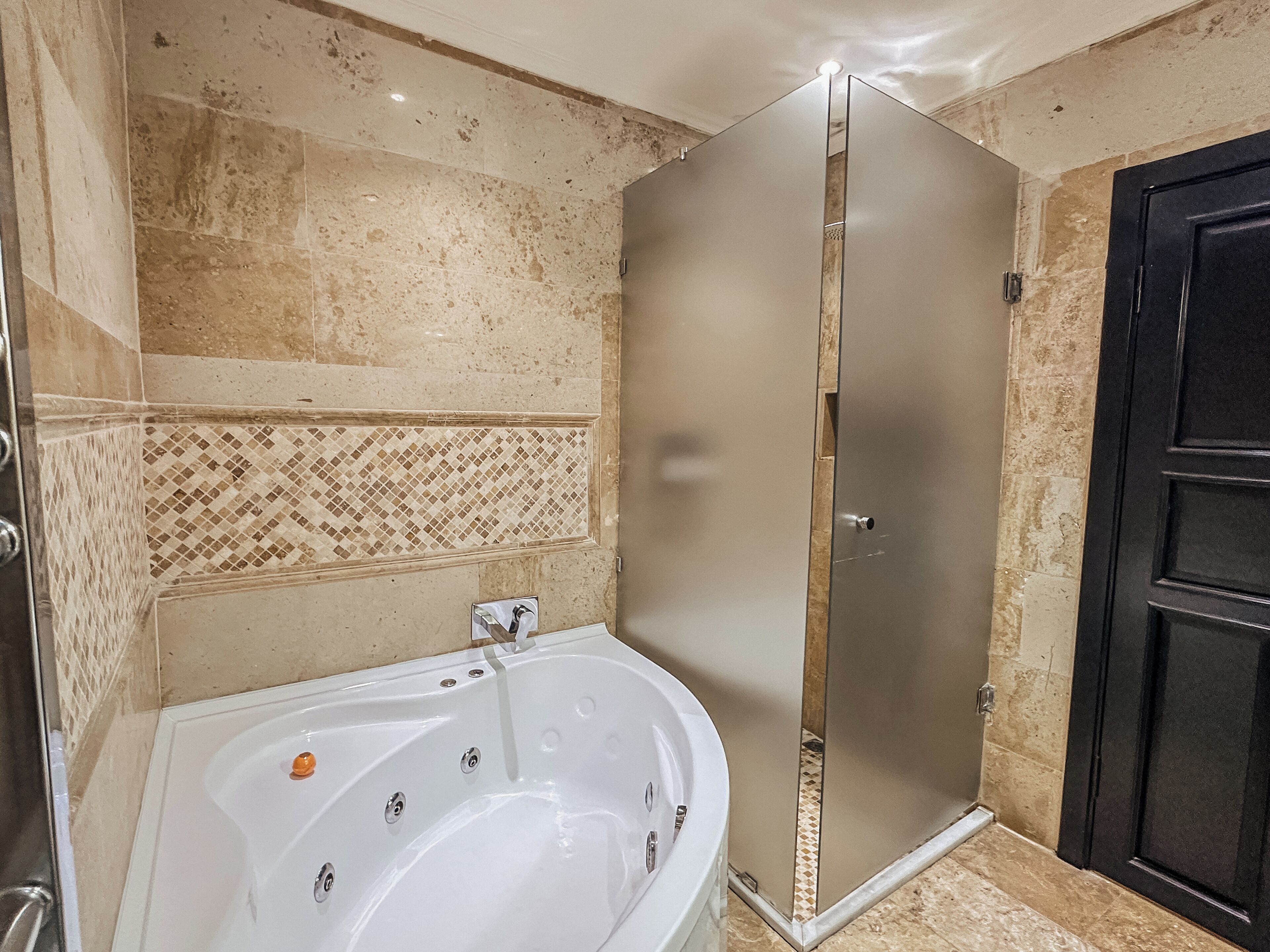 A bathroom with a white bathtub, a shower enclosure, and a tiled wall with a diamond pattern.
