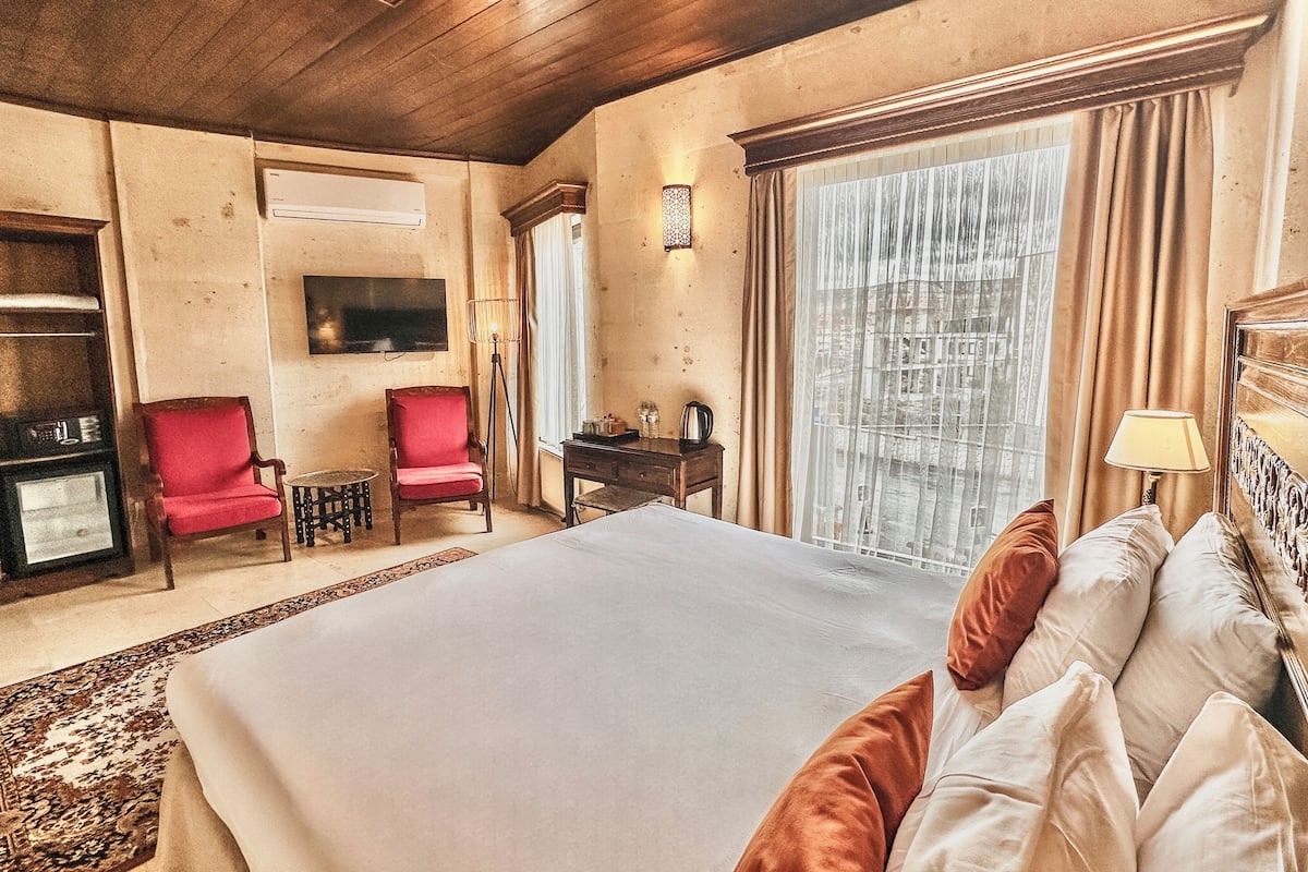 A hotel room with a large bed, a desk, a chair, a television, and a window with curtains.