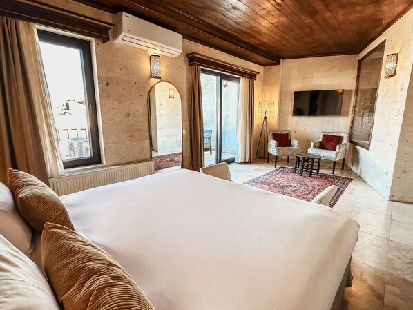 Habitación de hotel con una cama grande, una zona de estar con mesa y sillas, y un televisor montado en la pared.