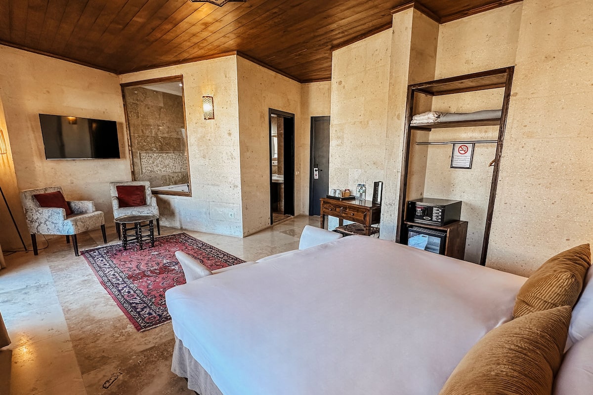 A hotel room with a bed, a desk, a chair, a TV, and a small table with a radio.