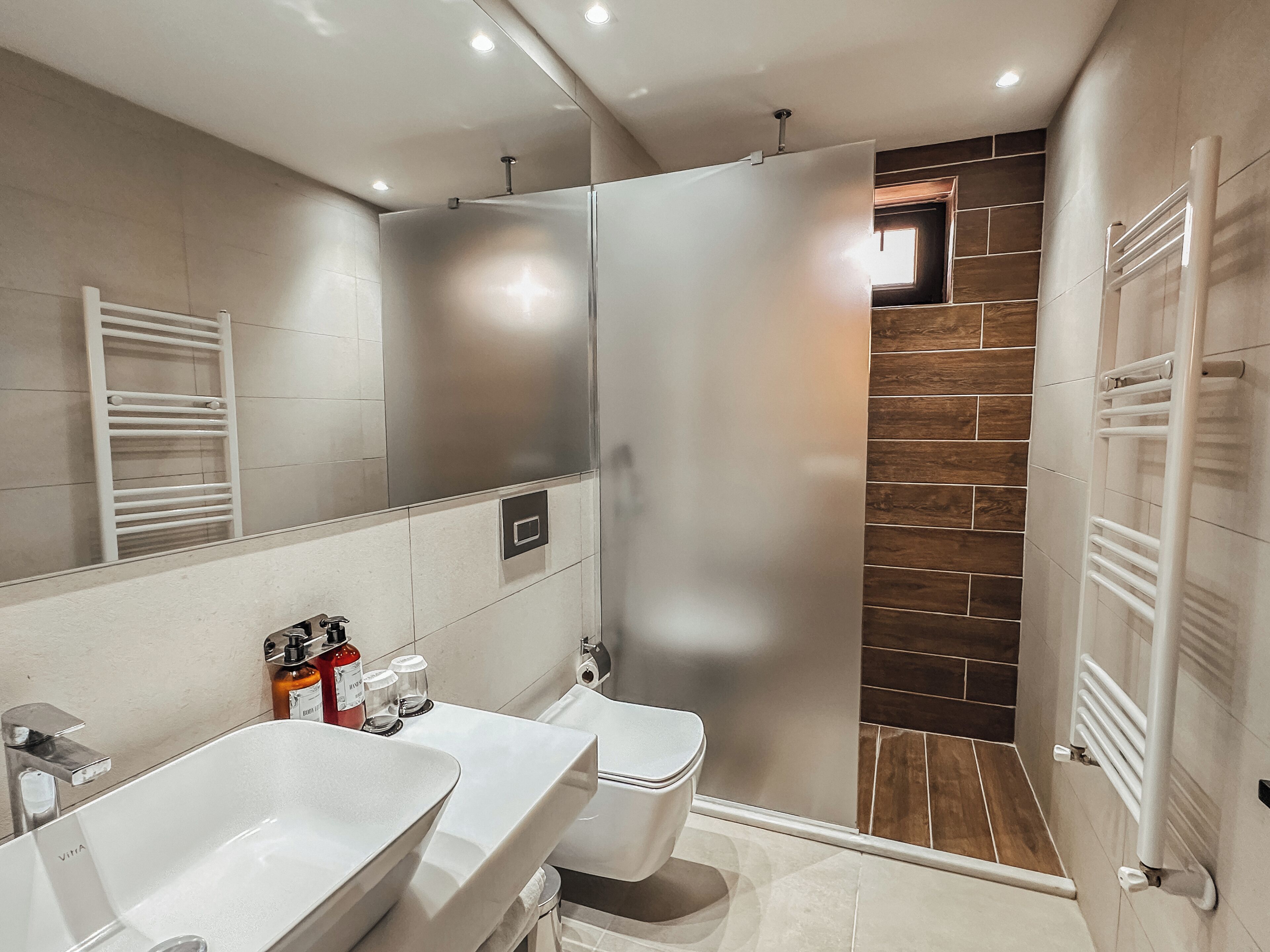 A modern bathroom with a shower, two sinks, a toilet, and a mirror.