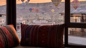 A view of hot air balloons over a mountainous landscape through a window with a striped cushion on a chair.